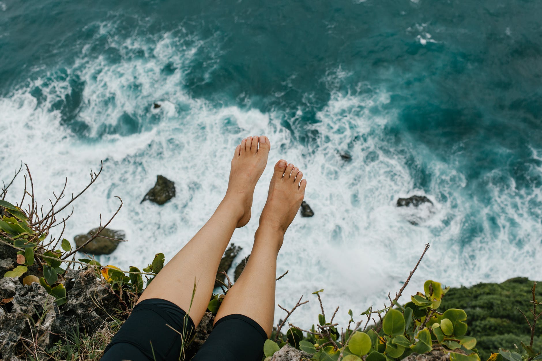 woman sitting on edge of cliff above foaming sea