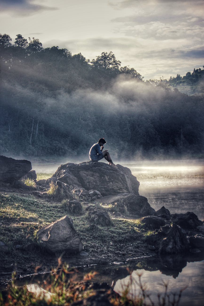 man in gray shit sitting on rock boulder